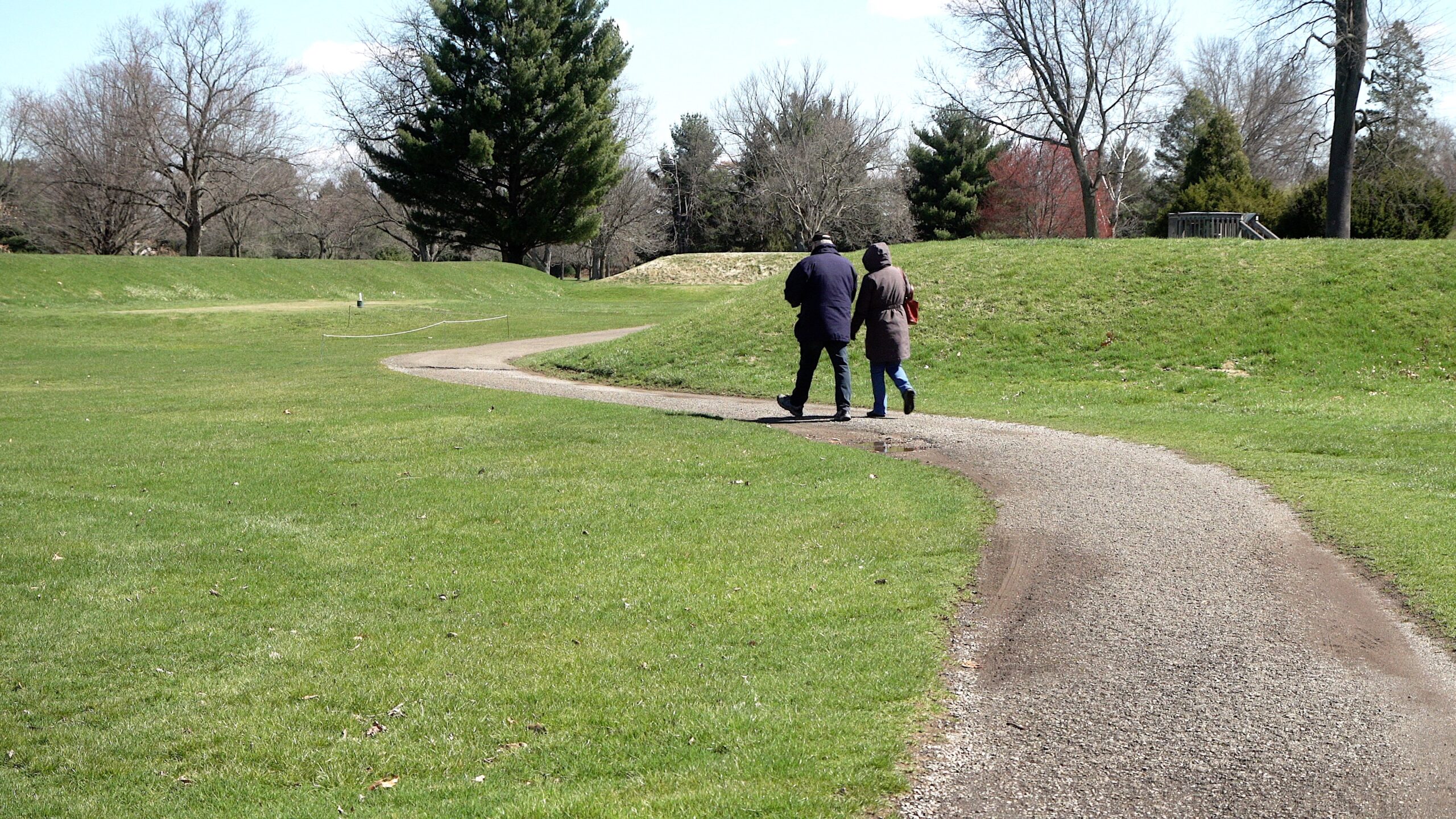 Two people walking between the mounds of the Octagon on a spring day. The words on the image say "The Octagon is now open"